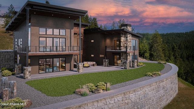 4663 E Plum Rd, Coeur Dalene, ID 83814 - back of house at dusk featuring a balcony, outdoor lounge area, a patio, a lawn, and stucco siding