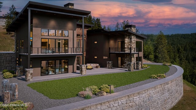 4663 E Plum Rd, Coeur Dalene, ID 83814 - back of house at dusk featuring a balcony, a chimney, outdoor lounge area, a patio, and a yard