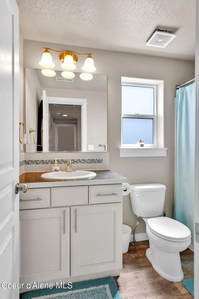3423 E Hope Ave, Post Falls, ID 83854 - bathroom featuring toilet, vanity, wood finished floors, decorative backsplash, and a textured ceiling