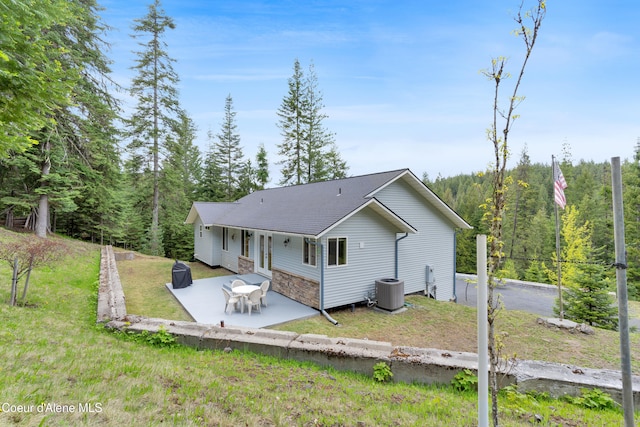 5340 W Hull Loop, Coeur Dalene, ID 83814 - back of house featuring a patio area, a lawn, stone siding, a wooded view, and a shingled roof
