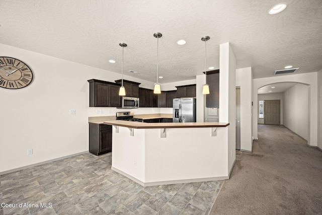 4717 N Connery Loop, Post Falls, ID 83854 - kitchen with appliances with stainless steel finishes, a breakfast bar, a textured ceiling, arched walkways, and dark brown cabinetry