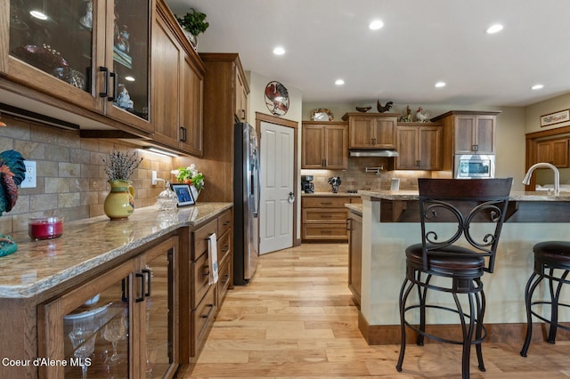 2795 Boekel Rd, Rathdrum, ID 83858 - kitchen featuring stainless steel appliances, a breakfast bar, light wood-style flooring, brown cabinets, and glass insert cabinets