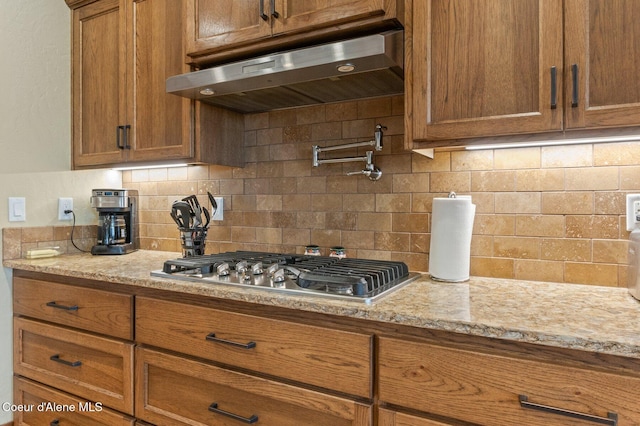 2795 Boekel Rd, Rathdrum, ID 83858 - kitchen with under cabinet range hood, stainless steel gas stovetop, brown cabinetry, and tasteful backsplash