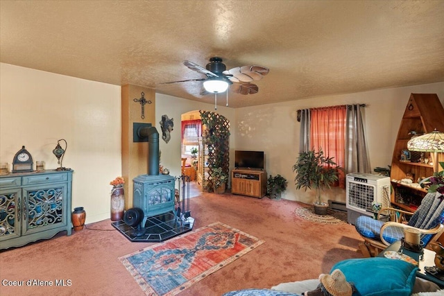 301 Third St, Osburn, ID 83849 - carpeted living room featuring a textured ceiling, a wood stove, ceiling fan, and a baseboard heating unit