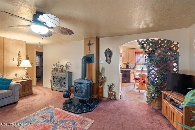 301 Third St, Osburn, ID 83849 - living area featuring light carpet, a textured ceiling, a ceiling fan, arched walkways, and a wood stove