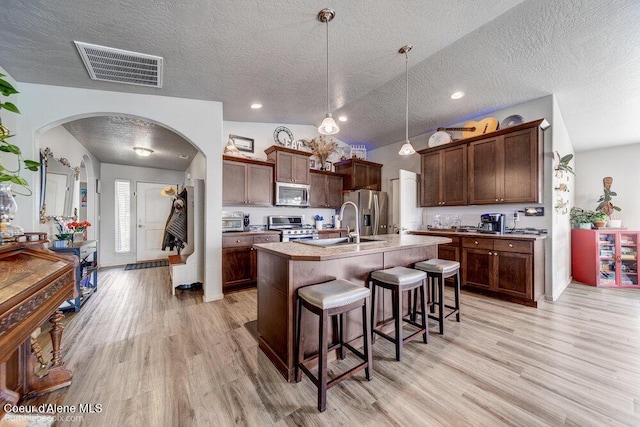 7156 W Christine St, Rathdrum, ID 83858 - kitchen with appliances with stainless steel finishes, arched walkways, a kitchen breakfast bar, light wood-style flooring, and a textured ceiling
