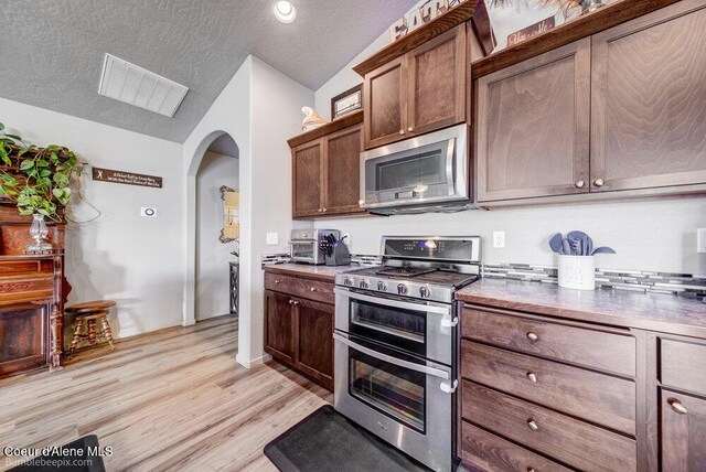 7156 W Christine St, Rathdrum, ID 83858 - kitchen with appliances with stainless steel finishes, vaulted ceiling, arched walkways, a textured ceiling, and light wood-style flooring