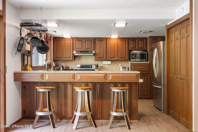 272 Hidden Springs Rd, Sandpoint, ID 83864 - kitchen with appliances with stainless steel finishes, under cabinet range hood, light wood-style floors, and a kitchen breakfast bar
