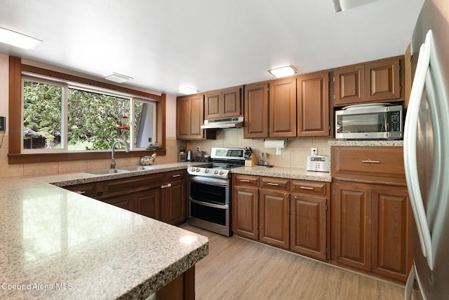 272 Hidden Springs Rd, Sandpoint, ID 83864 - kitchen featuring stainless steel appliances, under cabinet range hood, backsplash, a sink, and light wood-style floors