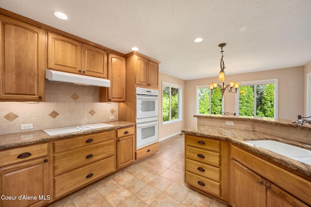 10016 N Zack Ct, Hayden, ID 83835 - kitchen featuring white appliances, under cabinet range hood, backsplash, light stone counters, and a chandelier