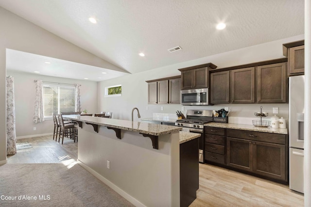 4447 N Connery Loop, Post Falls, ID 83854 - kitchen with appliances with stainless steel finishes, a breakfast bar, light stone countertops, dark brown cabinetry, and a center island with sink