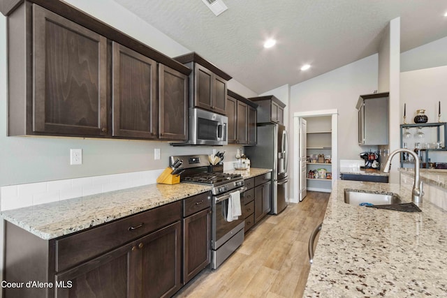 4447 N Connery Loop, Post Falls, ID 83854 - kitchen with appliances with stainless steel finishes, a sink, lofted ceiling, dark brown cabinetry, and light stone countertops