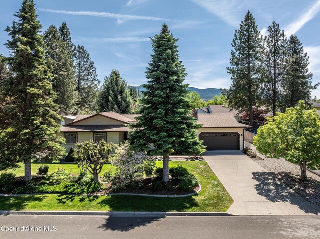 407 W Musket Ave, Post Falls, ID 83854 - view of property hidden behind natural elements featuring driveway, a garage, a front yard, and a mountain view