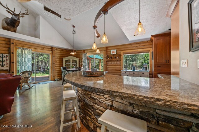 27294 N Clagstone Rd, Athol, ID 83801 - kitchen featuring log walls, a textured ceiling, dark wood-type flooring, dark stone countertops, and a breakfast bar