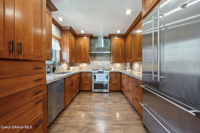 27294 N Clagstone Rd, Athol, ID 83801 - kitchen featuring stainless steel appliances, wall chimney range hood, a sink, brown cabinetry, and light stone counters