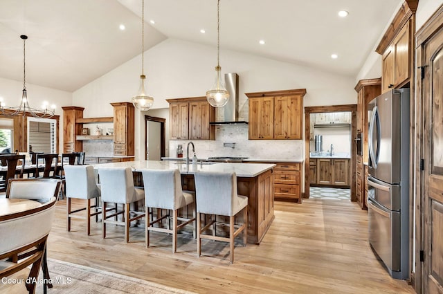 11690 N Arnicas Ct, Hayden, ID 83835 - kitchen featuring wall chimney range hood, freestanding refrigerator, a large island with sink, a chandelier, and brown cabinets
