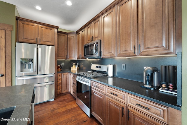 11387 N Armonia Way, Hayden Lake, ID 83835 - kitchen featuring stainless steel appliances, dark countertops, dark wood-type flooring, brown cabinetry, and recessed lighting