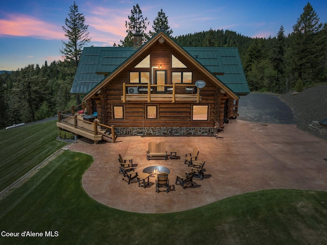 17442 S Painted Rose Rd, Worley, ID 83876 - back of house at dusk featuring an outdoor fire pit, a lawn, a patio area, a chimney, and a wooded view