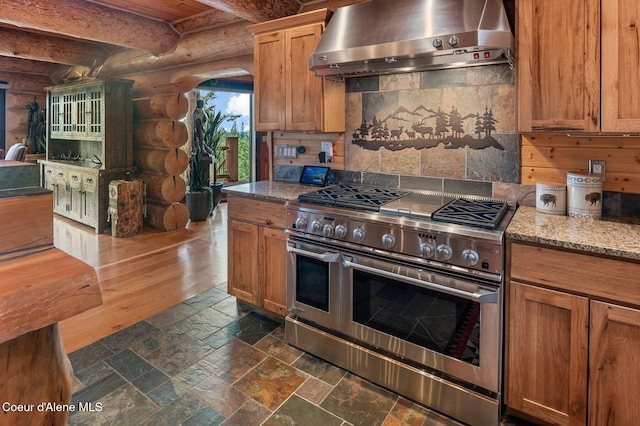 17442 S Painted Rose Rd, Worley, ID 83876 - kitchen with range with two ovens, wall chimney exhaust hood, rustic walls, tasteful backsplash, and beamed ceiling