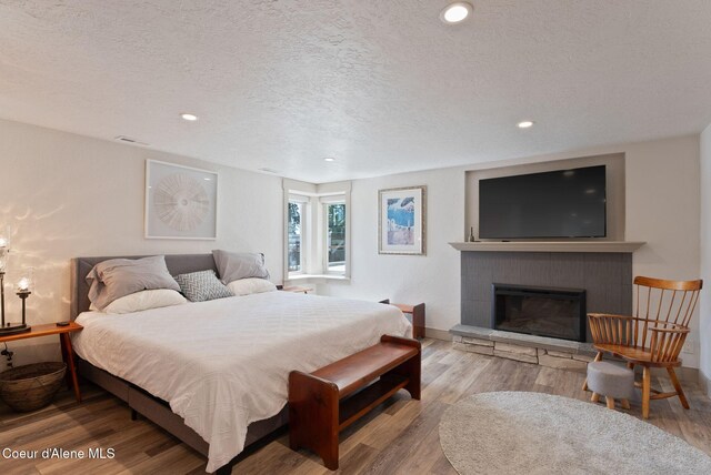 2406 S Silver Beach Rd, Coeur Dalene, ID 83814 - bedroom featuring a textured ceiling, wood finished floors, recessed lighting, a glass covered fireplace, and baseboards