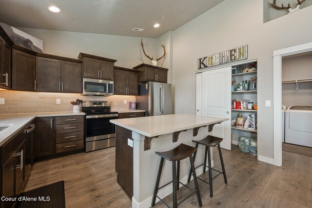 27968 N Timber Ridge Rd, Rathdrum, ID 83858 - kitchen featuring appliances with stainless steel finishes, dark brown cabinets, a breakfast bar area, decorative backsplash, and a kitchen island