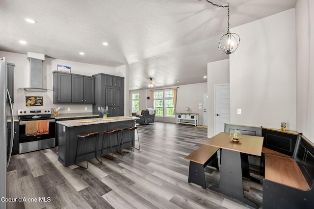 1446 Sagle Creek Rd, Sagle, ID 83860 - kitchen featuring appliances with stainless steel finishes, wall chimney range hood, a center island, a kitchen bar, and wood finished floors