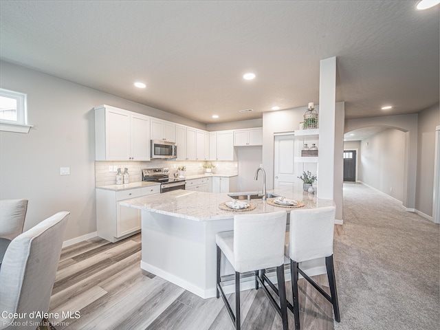 13668 N Apex Way, Hayden, ID 83835 - kitchen featuring appliances with stainless steel finishes, arched walkways, light stone counters, a sink, and white cabinets