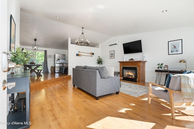 9298 N Clarkview Pl, Hayden, ID 83835 - living room featuring vaulted ceiling, light wood-type flooring, a glass covered fireplace, a wall mounted AC, and a chandelier