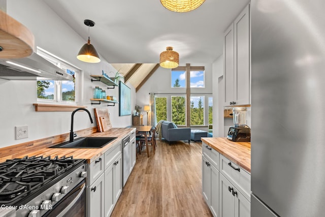 723 Trout Crk Rd, Sandpoint, ID 83864 - kitchen featuring wooden counters, appliances with stainless steel finishes, wall chimney exhaust hood, light wood finished floors, and hanging light fixtures