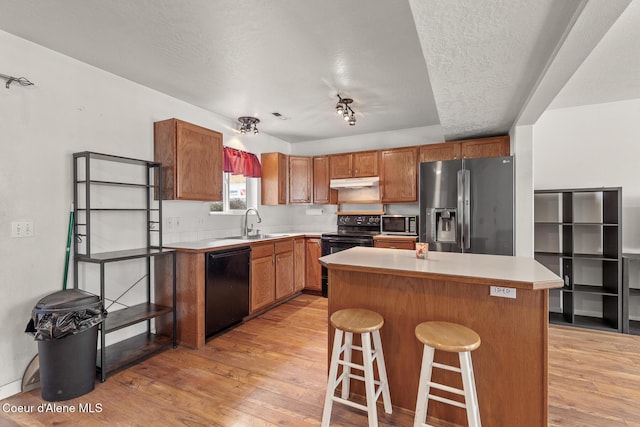 6687 W Flagstaff St, Rathdrum, ID 83858 - kitchen with black appliances, light wood-style flooring, a kitchen island, a sink, and a kitchen bar
