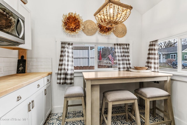 721 N A St, Coeur Dalene, ID 83814 - kitchen with stainless steel microwave, decorative backsplash, white cabinets, vaulted ceiling, and baseboards