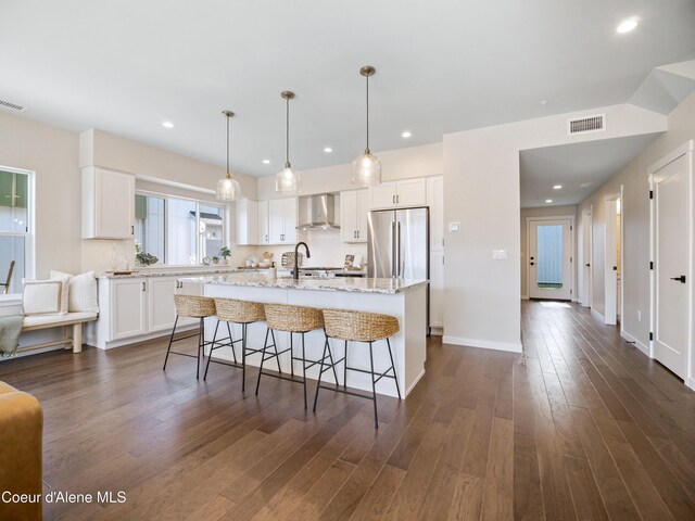 1031 E Railroad Ave, Post Falls, ID 83854 - kitchen with wall chimney range hood, a center island with sink, dark wood-style flooring, white cabinets, and stainless steel fridge