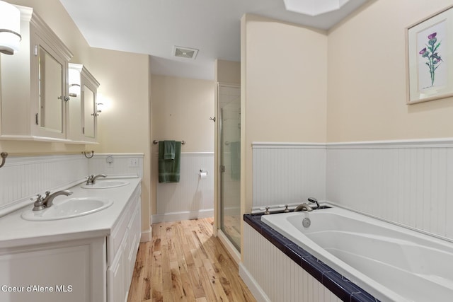 8511 N Summerfield Loop, Hayden, ID 83835 - bathroom featuring wood finished floors, a wainscoted wall, a bath, double vanity, and a stall shower