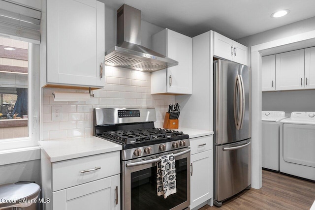 228 Snowgoose Ln Unit 8, Sandpoint, ID 83864 - kitchen featuring stainless steel appliances, wall chimney exhaust hood, separate washer and dryer, wood finished floors, and white cabinetry