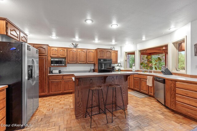 15248 N Atlas Rd, Rathdrum, ID 83858 - kitchen featuring appliances with stainless steel finishes, a breakfast bar, brown cabinets, light countertops, and a sink
