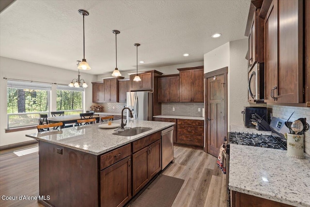 23378 N Prominence Rd, Rathdrum, ID 83858 - kitchen featuring appliances with stainless steel finishes, light wood-type flooring, a textured ceiling, decorative backsplash, and an island with sink