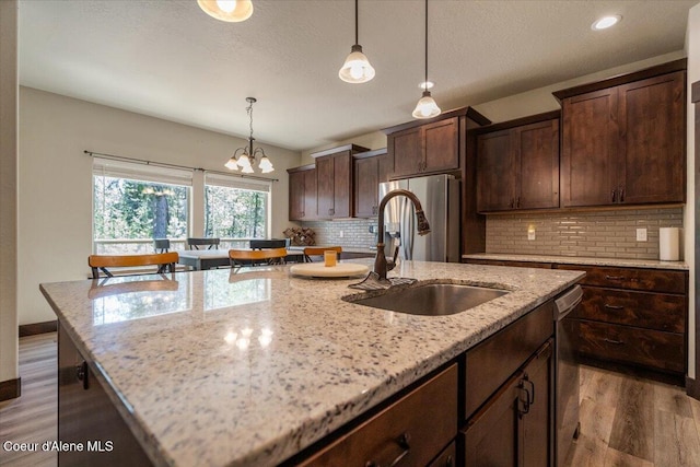 23378 N Prominence Rd, Rathdrum, ID 83858 - kitchen featuring wood finished floors, a kitchen island with sink, tasteful backsplash, stainless steel appliances, and light stone counters
