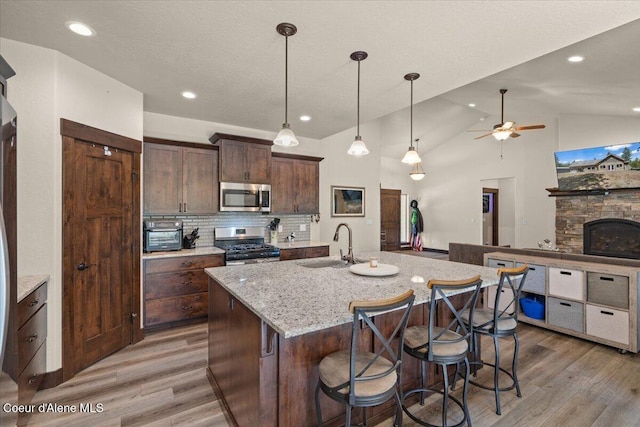 23378 N Prominence Rd, Rathdrum, ID 83858 - kitchen with stainless steel appliances, light wood-style floors, a ceiling fan, a center island with sink, and light stone counters