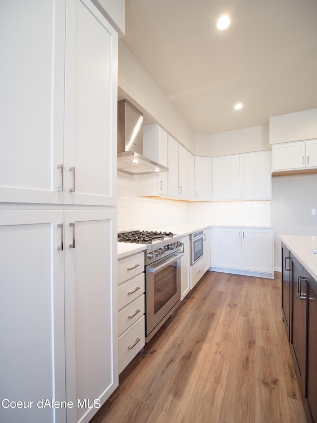 1048 E 4th Ave, Post Falls, ID 83854 - kitchen with wall chimney range hood, gas range, light wood-style flooring, white cabinetry, and recessed lighting
