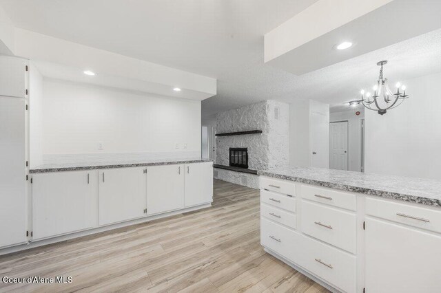 16 Beers Humbird Rd, Sagle, ID 83860 - kitchen with white cabinets, a fireplace, light wood-type flooring, a chandelier, and recessed lighting