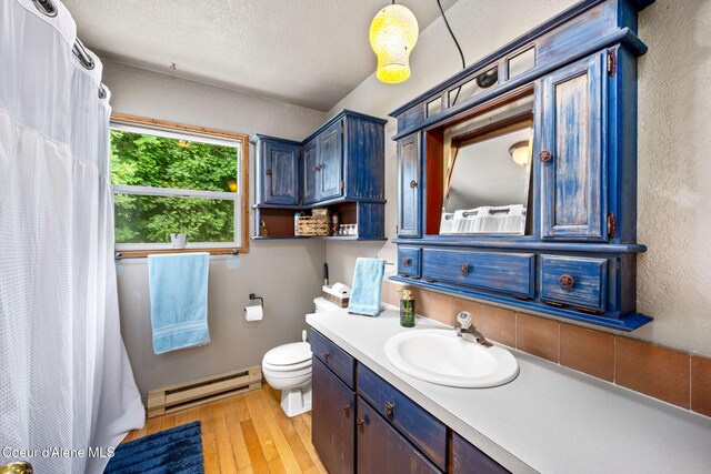 8525 W Nevada St, Rathdrum, ID 83858 - full bathroom featuring a baseboard heating unit, wood finished floors, vanity, a textured wall, and toilet