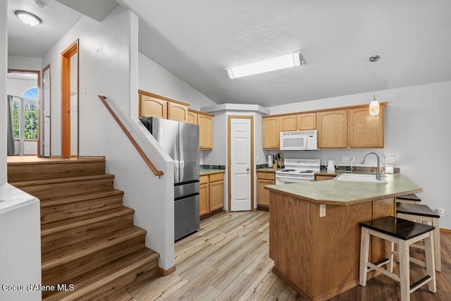 5735 E Steamboat Bnd, Post Falls, ID 83854 - kitchen featuring white appliances, a sink, a peninsula, light wood-style flooring, and a breakfast bar