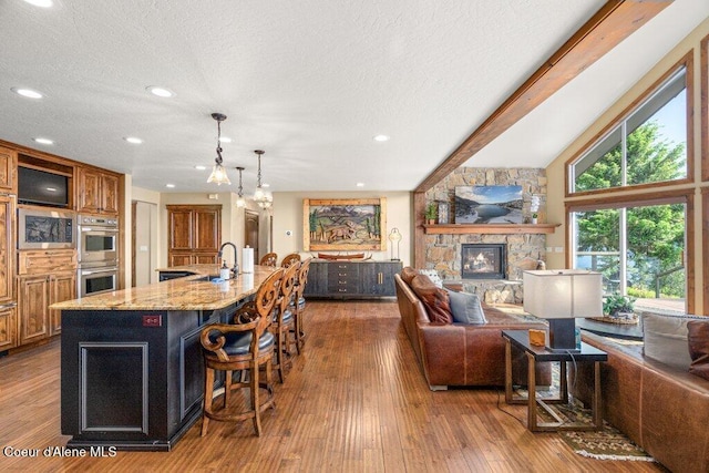 4987 S Bay Pointe Way, Coeur Dalene, ID 83814 - kitchen featuring appliances with stainless steel finishes, open floor plan, a breakfast bar area, a stone fireplace, and light stone counters