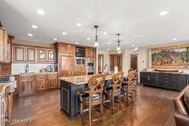4987 S Bay Pointe Way, Coeur Dalene, ID 83814 - kitchen with brown cabinets, a sink, recessed lighting, light stone countertops, and a kitchen breakfast bar