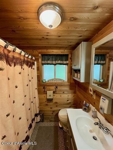 22767 Spruce Ln, Lewiston, ID 83501 - bathroom with wood ceiling, toilet, vanity, wooden walls, and a shower with curtain