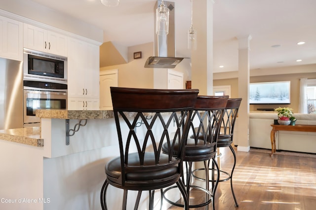 13 Park Dr, Spirit Lake, ID 83869 - kitchen featuring stainless steel oven, built in microwave, a breakfast bar, island exhaust hood, and white cabinets