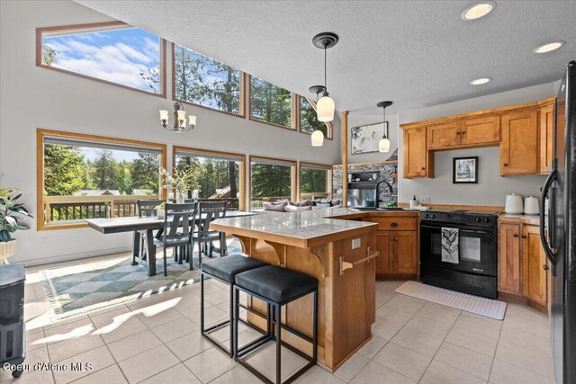 106 Stewart Dr, Blanchard, ID 83804 - kitchen featuring black appliances, a chandelier, a kitchen breakfast bar, light tile patterned flooring, and brown cabinetry