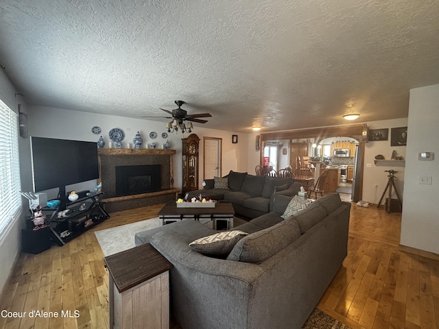 9670 N Meadow Way, Hayden, ID 83835 - living room with a textured ceiling, a ceiling fan, light wood-style flooring, and a fireplace with raised hearth