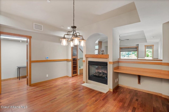 303 S 11th St, Coeur Dalene, ID 83814 - unfurnished living room featuring wood finished floors, ceiling fan, arched walkways, baseboards, and a multi sided fireplace