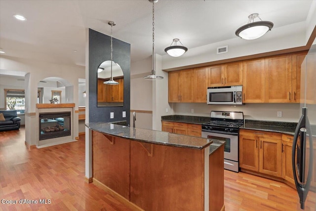303 S 11th St, Coeur Dalene, ID 83814 - kitchen with appliances with stainless steel finishes, dark stone counters, brown cabinetry, arched walkways, and light wood-style floors